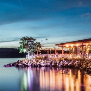 the outdoor deck at The Hudson is lit up at twilight, and the lights reflect on The Hudson River right next to the venue itself