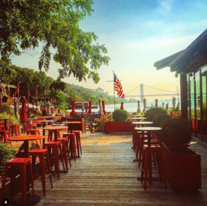 the outdoor deck at The Hudson in the late afternoon. The George Washington Bridge is in the background